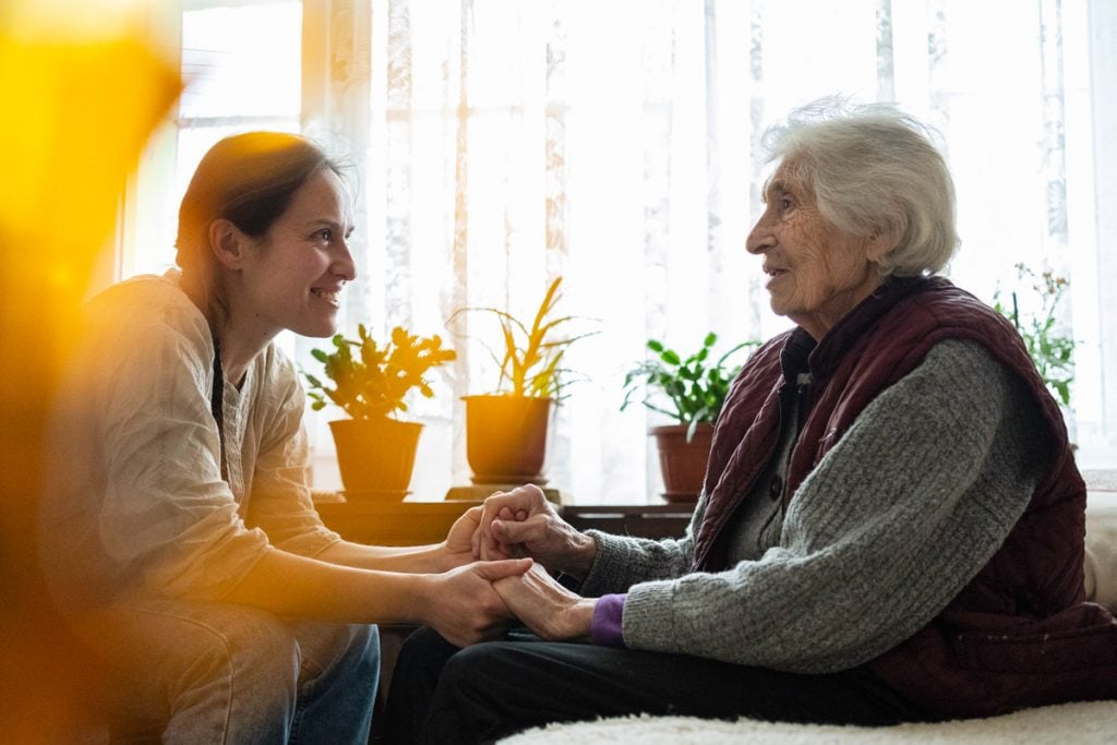 A college age person holds hands with an elderly woman.